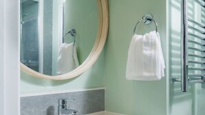 Een badkamer met een witte wastafel, een houten wastafelmeubel, een ronde spiegel en een handdoekhouder.
