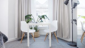 Een kamer met een witte tafel, twee witte stoelen, een plant in pot, een vloerlamp en een raam met gordijnen.