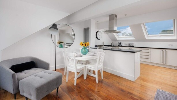 Eine moderne Küche mit Dachfenster, weißen Schränken und einem Essbereich mit grauem Sofa und weißen Stühlen.