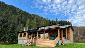 Eine Holzhütte mit Veranda, Treppe und Blick auf einen bewaldeten Berg.