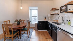 Una cocina con mesa de madera, sillas, una ventana, armarios negros, un lavamanos de acero inoxidable y una lámpara colgante.