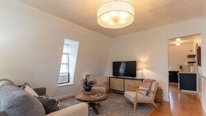 Una sala de estar con sofá, sillón, mesa de centro, televisión y una cocina al fondo.