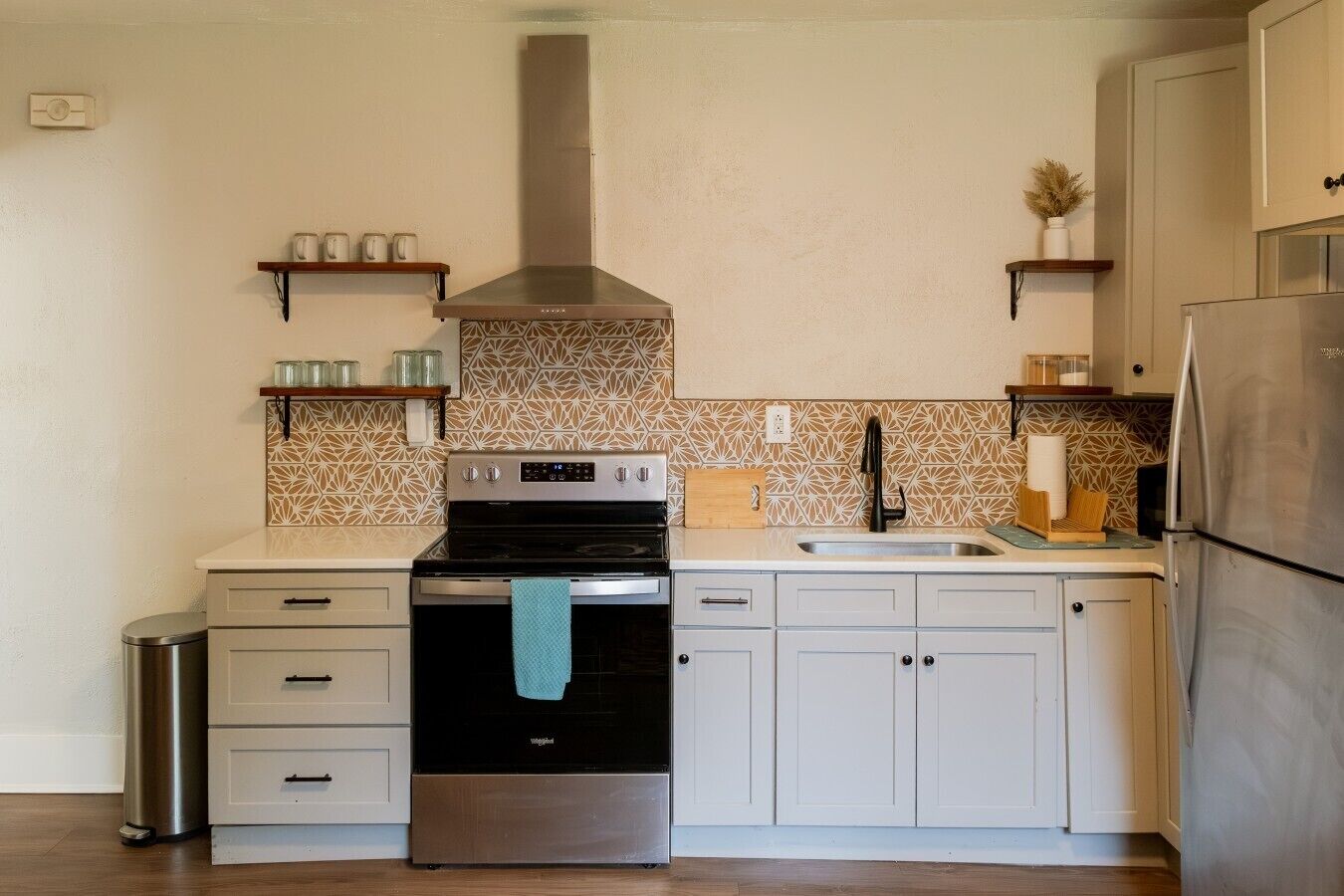 A kitchen with a stainless steel stove, a sink, and a refrigerator. There are cabinets and a countertop.