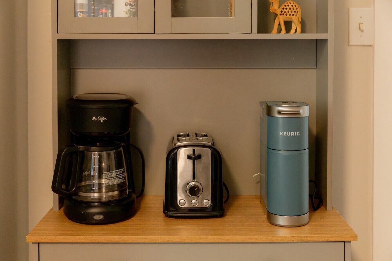A kitchenette with a coffee maker, toaster, and a water bottle on a wooden countertop.
