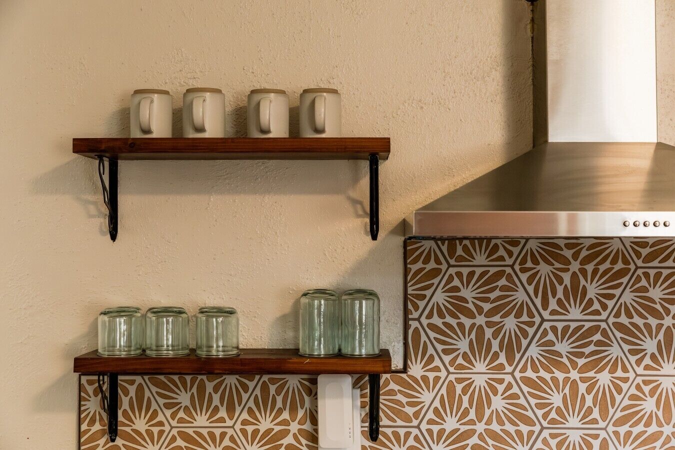 Deux étagères en bois, sur lesquelles sont posées des tasses et des bocaux en verre, sont adossées à un mur texturé, et un pare-feu décoratif complète l'ensemble.