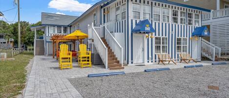 A building with a blue and white exterior, a covered outdoor seating area with yellow chairs, and a staircase leading to the entrance.