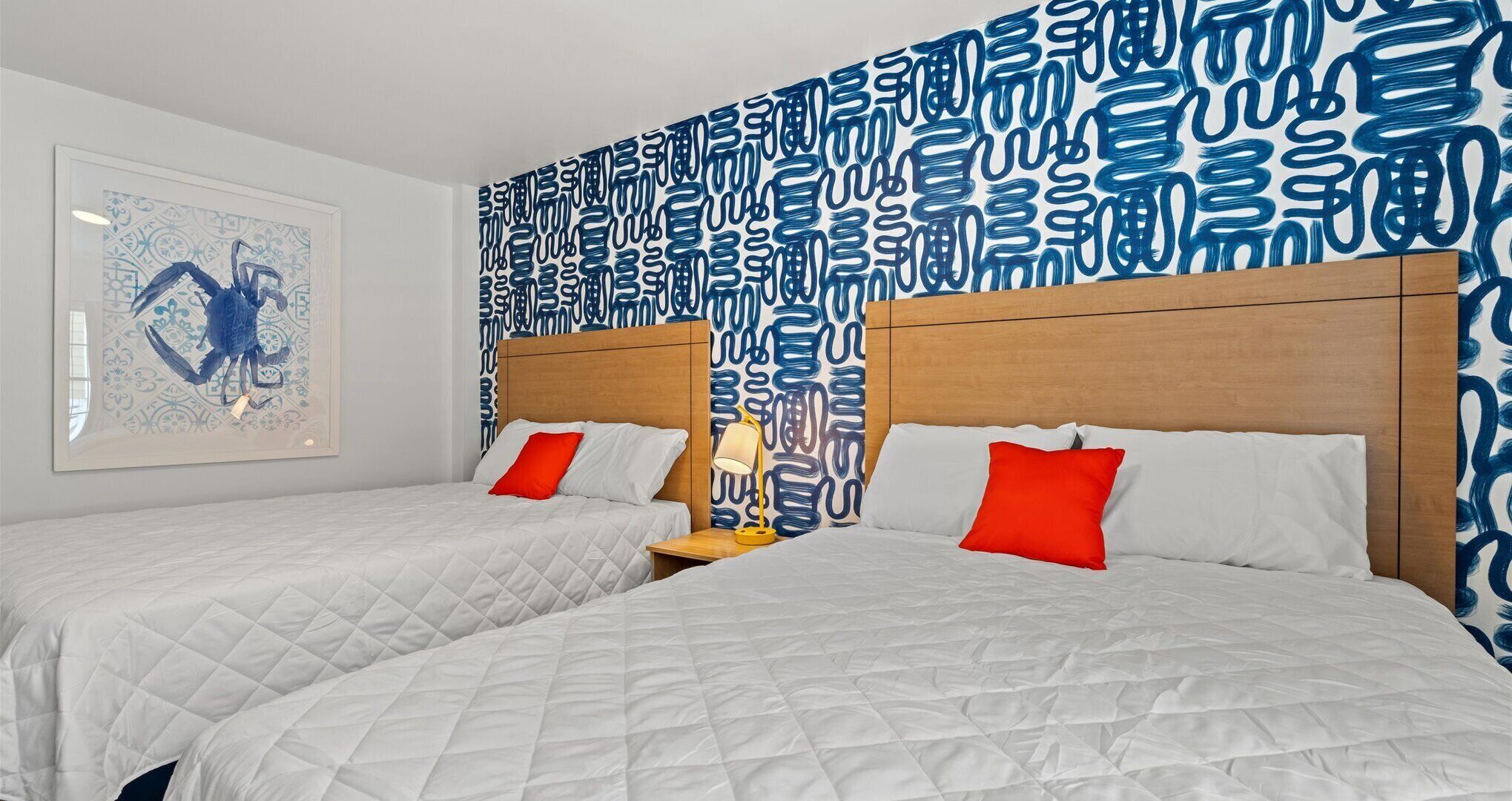 A hotel room with two beds, a wooden headboard, a patterned wall, and a framed artwork.