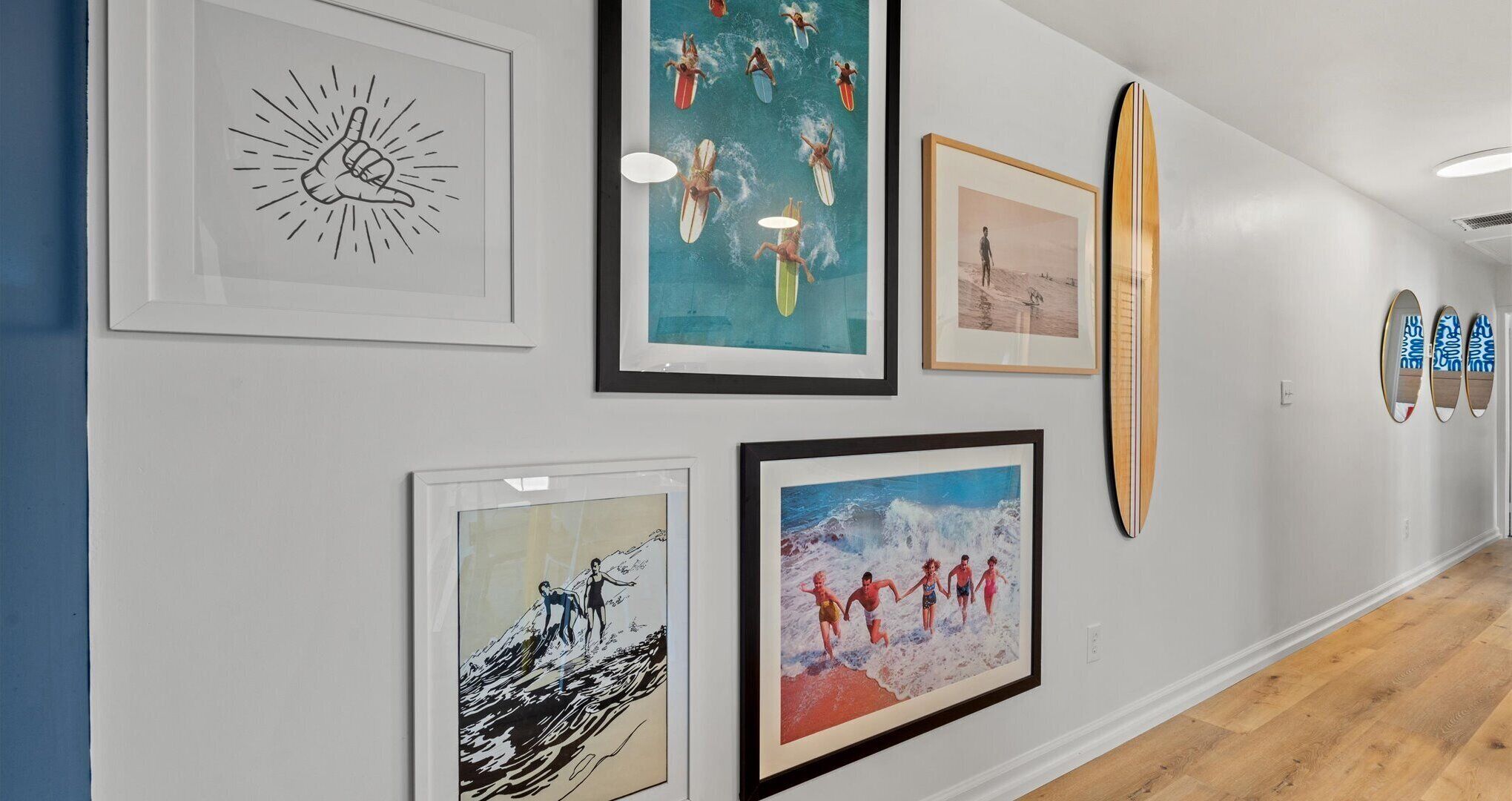 Um corredor com obras emolduradas nas paredes, incluindo uma ilustração de sol, uma cena de praia e uma imagem de surf.