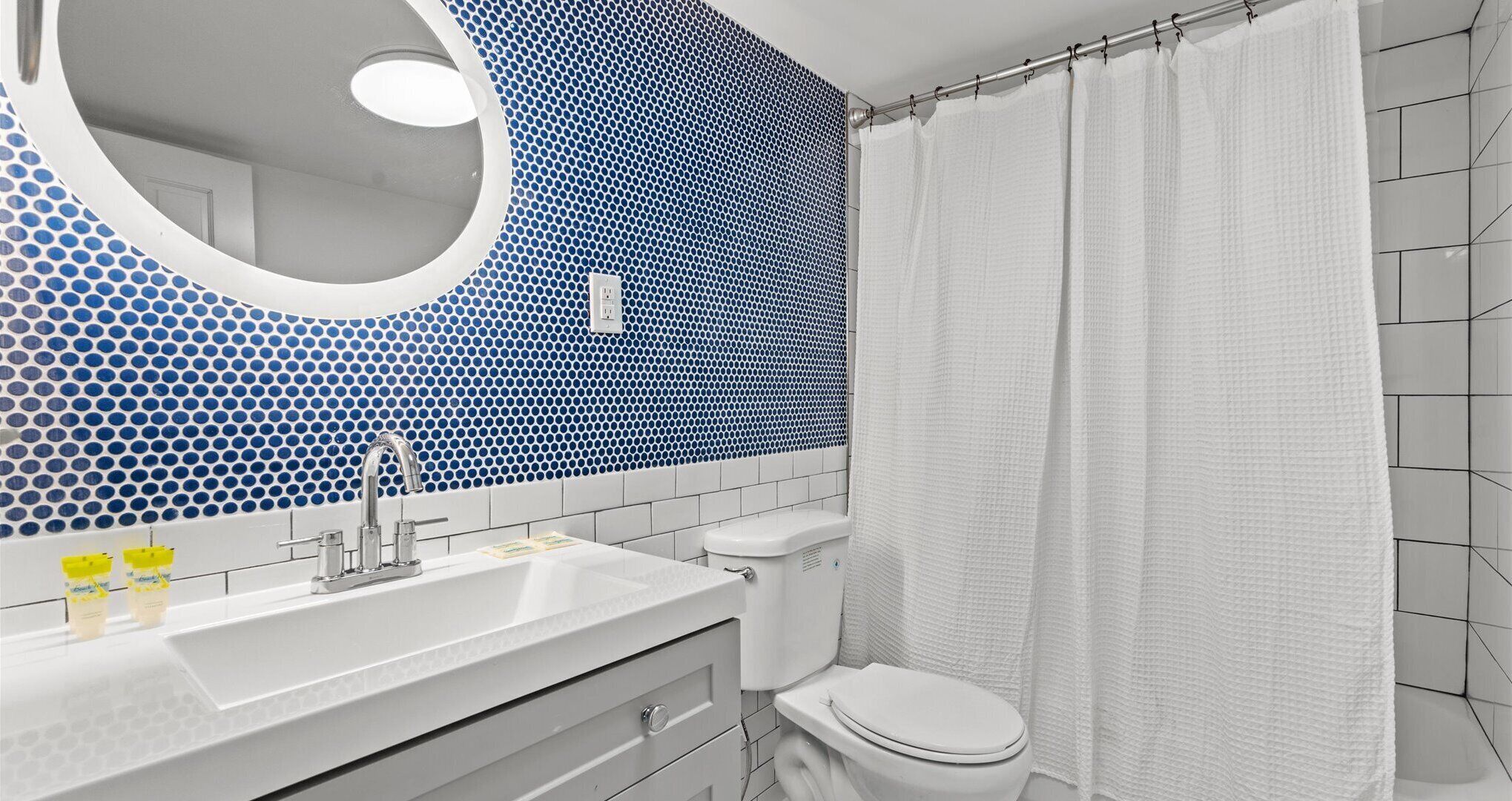 A bathroom with a sink, mirror, toilet, and shower curtain.