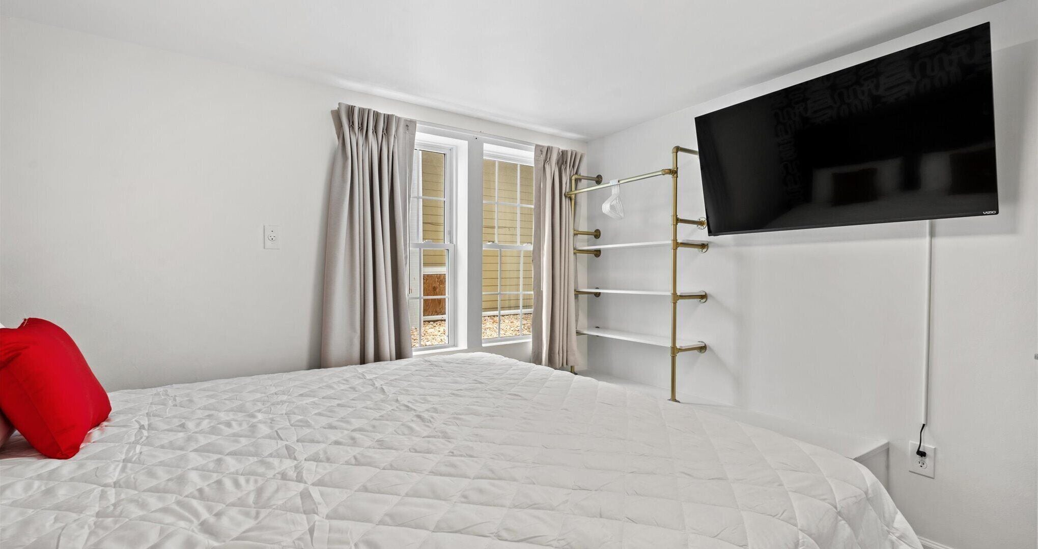 A bedroom with a bed, a TV mounted on the wall, and a window with curtains.
