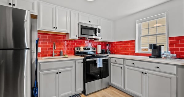 A modern kitchen with white cabinets, a stainless steel refrigerator, a black oven, and a red-tiled backsplash. - Cabana Beach - RR Beach Club LLC (North Myrtle Beach)