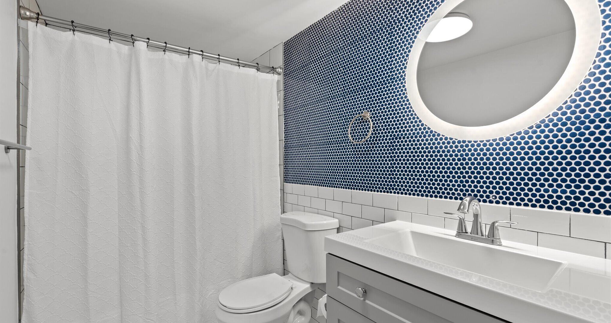 Un baño con inodoro blanco, lavamanos con grifo moderno y cortina de ducha.