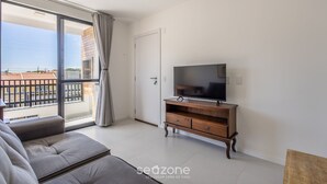 Ein modernes Wohnzimmer mit einer Couch, einem Fernseher auf einem Holzschrank und einer Glastür, die auf einen Balkon führt.