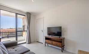 Un soggiorno moderno con un divano, una TV su un mobile in legno e una porta scorrevole in vetro che dà su un balcone.