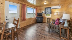 Een houten blokhut interieur met een eettafel, stoelen, een bank, een televisie en een kleine keukenhoek.