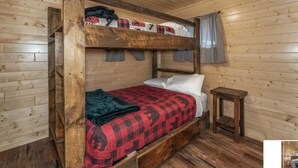 Een stapelbed met een rood-zwarte spreideken, een houten hoofdbord en een klein nachtkastje van hout.
