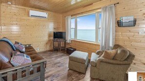 A wooden cabin interior with a sofa, armchair, ottoman, and a television on a wooden stand. - Hillside Resort Cabin #4 (Phelps)