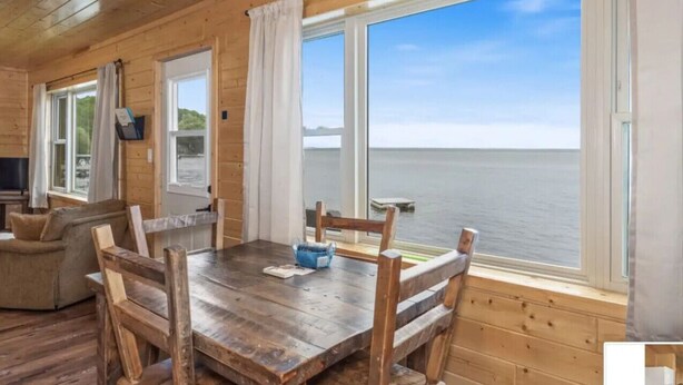 A wooden cabin with a dining table, chairs, and a view of the water. - Hillside Resort Cabin #4 (Phelps)
