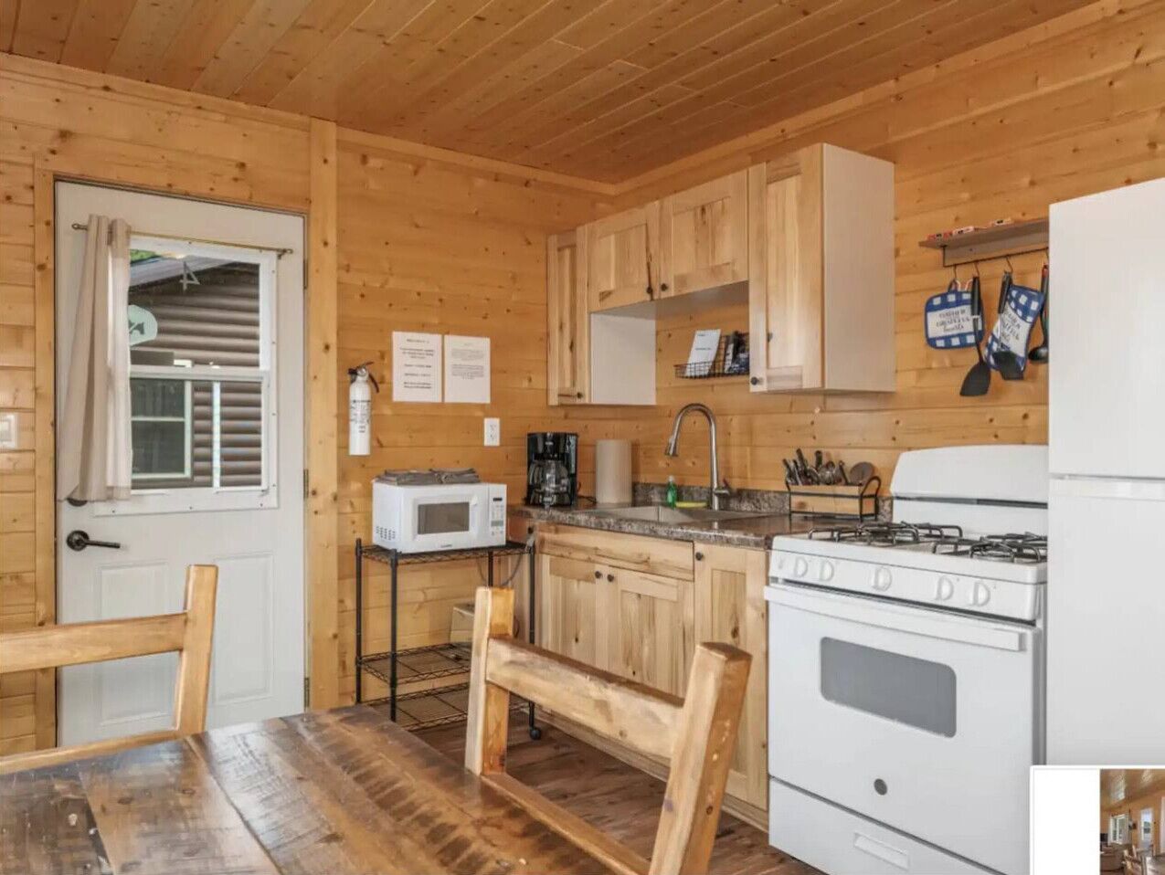 Une cuisine de style rustique, avec des murs en bois, un poêle blanc, un four à micro-ondes et des armoires en bois.