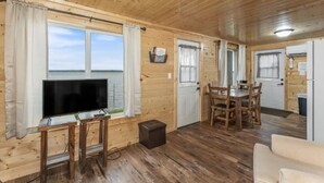 Eine Holzhütte mit Fernseher auf einem Schrank, einem Essbereich und einer Küche.