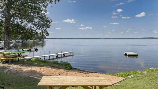 Ein Picknickplatz am Seeufer mit einem Holztisch, Bänken, einem Steg und einem Boot.