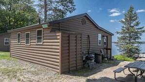 Eine Blockhütte mit einer kleinen Veranda, einem Grill und einem Picknicktisch.