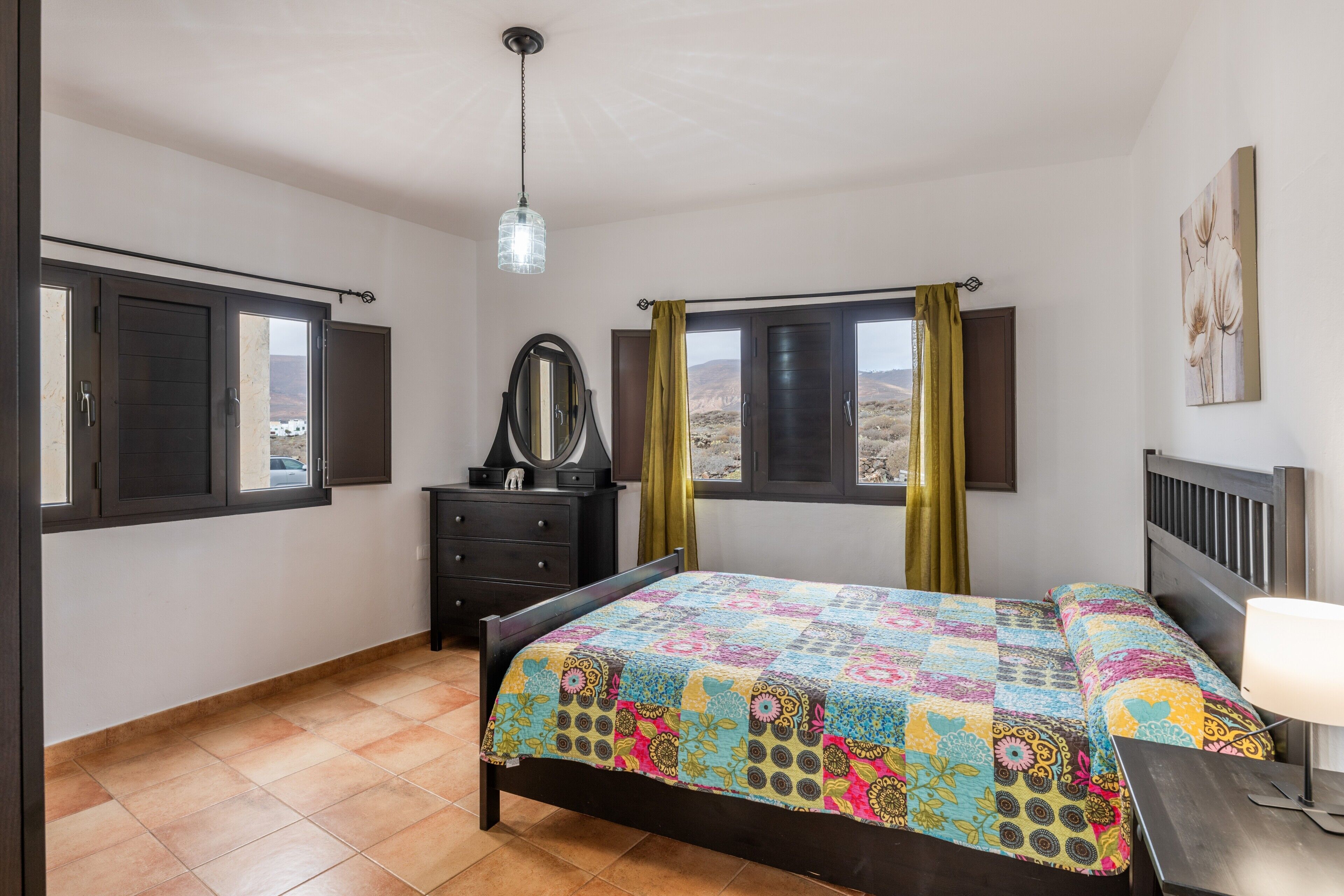 A bedroom with a bed, a dresser, a mirror, and a window with curtains.