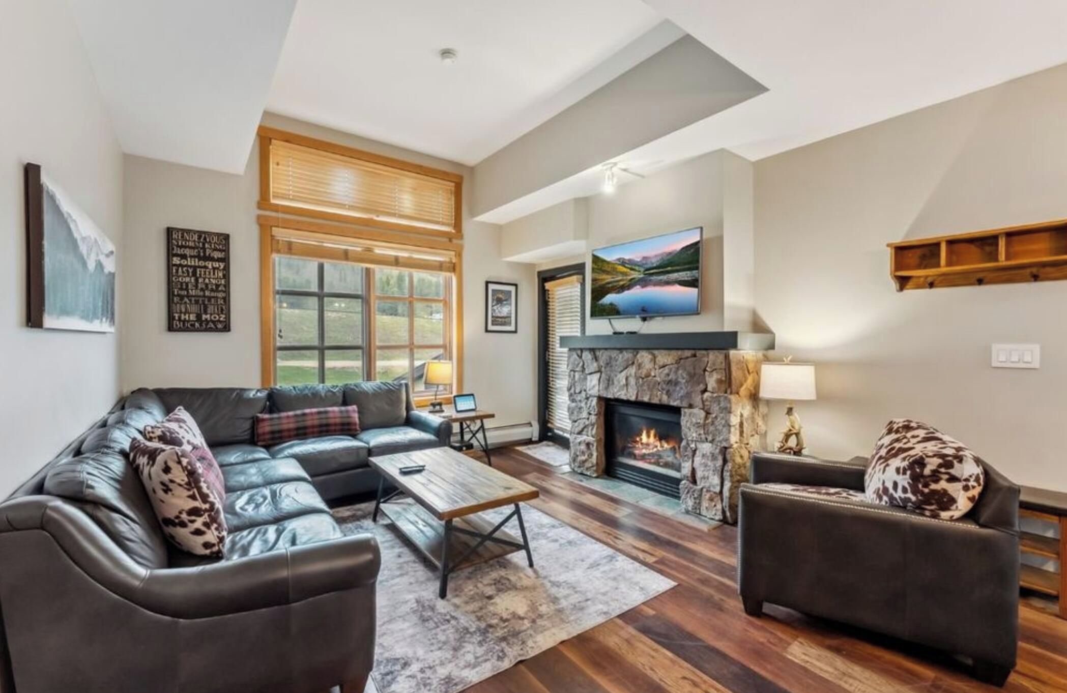 A spacious living room with a fireplace, leather sofas, and a large window.