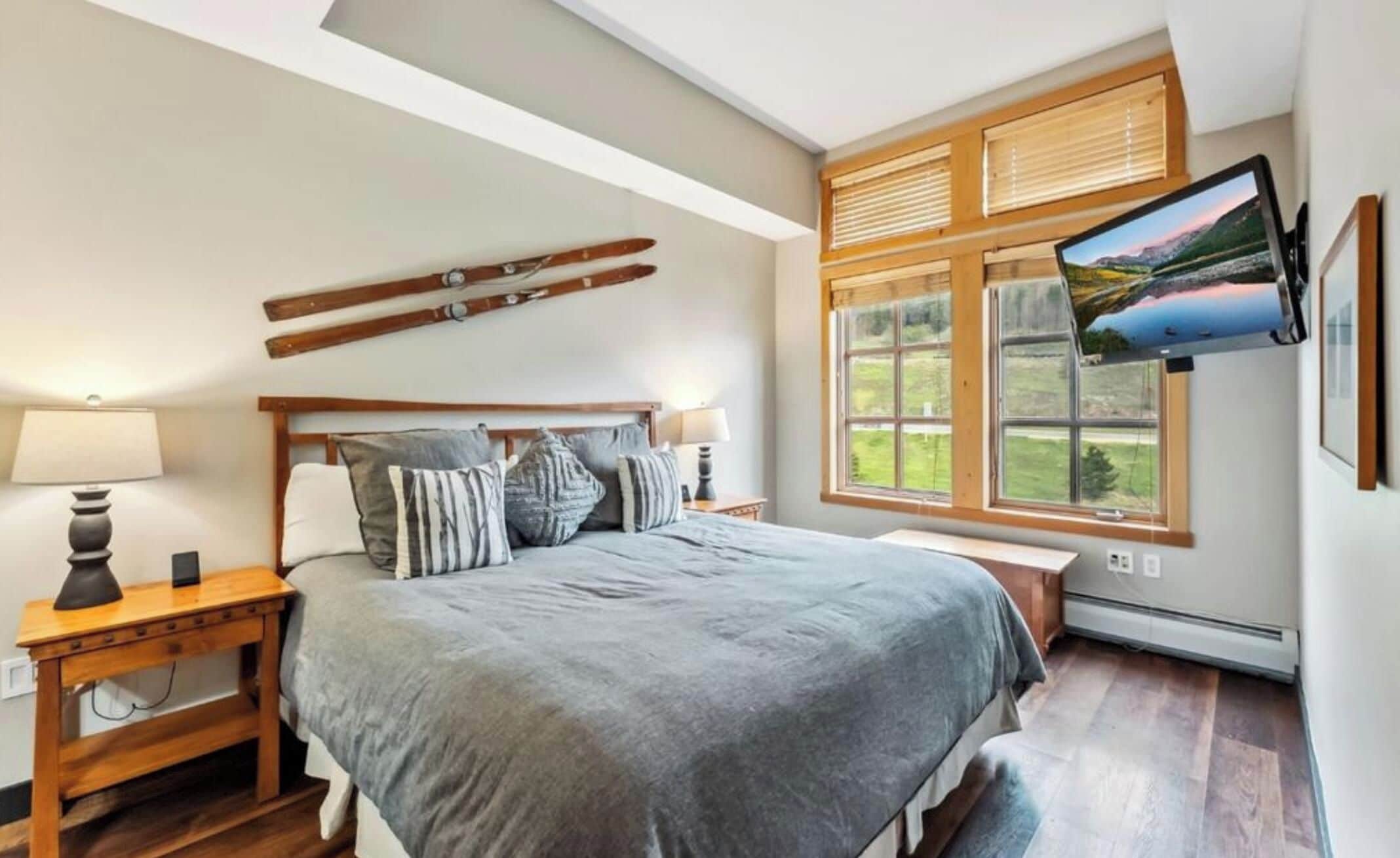 A bedroom with a bed, bedside tables, a TV, and a window with blinds.