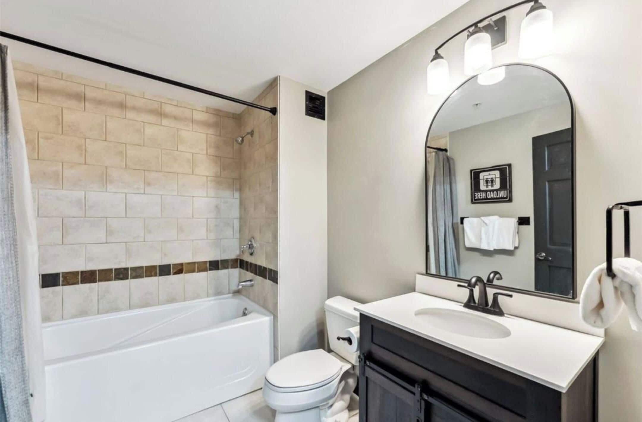 A modern bathroom with a bathtub, toilet, sink, and a large mirror.