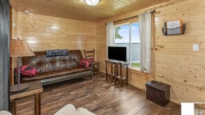 A cozy cabin interior with a leather sofa, a TV on a wooden stand, and a window with curtains.