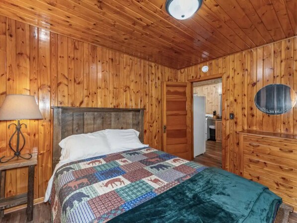 Une pièce aux murs lambrissés, avec un lit, une table de chevet dotée d’une lampe et un miroir rond accroché au mur.