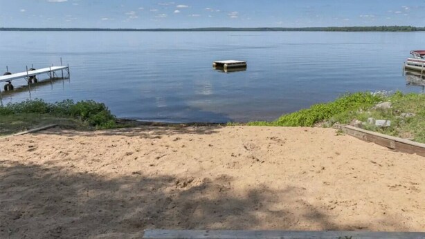 Ein Sandstrand mit einer Anlegestelle und einem kleinen Boot im Wasser.
