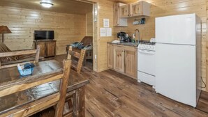 Ein Holzinnenraum mit Esstisch, Stühlen, einer Küchenzeile mit Herd und Kühlschrank sowie einem Fernseher in der Ecke.