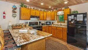 A kitchen with wooden cabinets, granite countertops, a black refrigerator, and a stove. - Cabin #12 Thunder Bay Resort (Phelps)