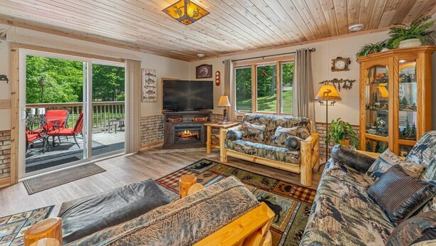 A cozy living room with a fireplace, comfortable seating, and a large window offering a view of greenery. - Cabin #12 Thunder Bay Resort (Phelps)