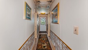 A narrow hallway with wooden beams on the ceiling, a patterned rug on the floor, and framed pictures on the walls. - Cabin #12 Thunder Bay Resort (Phelps)