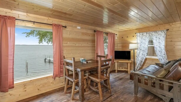 Eine Holzhütte mit rustikalem Interieur, einem Esstisch mit Stühlen, einer Couch und einem Fernseher.