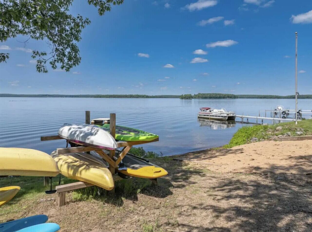 Paisaje junto al lago con kayaks y un bote amarrado en un muelle.