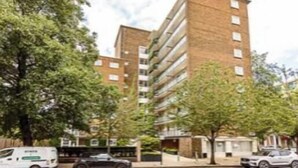 Un immeuble moderne à plusieurs étages, doté d’une façade en briques, entouré d’arbres et bordé de voitures garées.