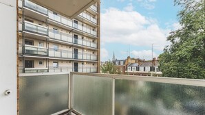 Un balcon donnant sur un immeuble résidentiel à plusieurs étages, avec un ciel dégagé et un arbre.
