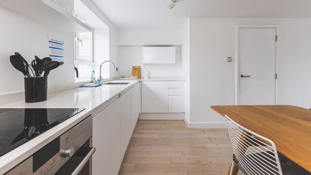 Une cuisine moderne avec des meubles blancs, une table à manger en bois et un four encastré.