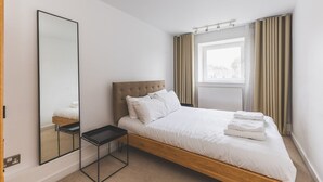 Une chambre d’hôtel moderne avec un grand lit, une table de chevet, un miroir et une fenêtre avec des rideaux.