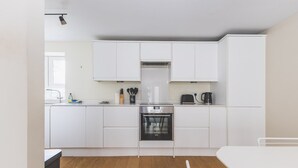 A modern kitchen with white cabinets, a stainless steel oven, and a coffee maker. - 2BR Central Belgravia Retreat (London)