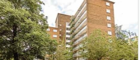 A modern multi-story building with a brick facade, surrounded by trees and parked cars.