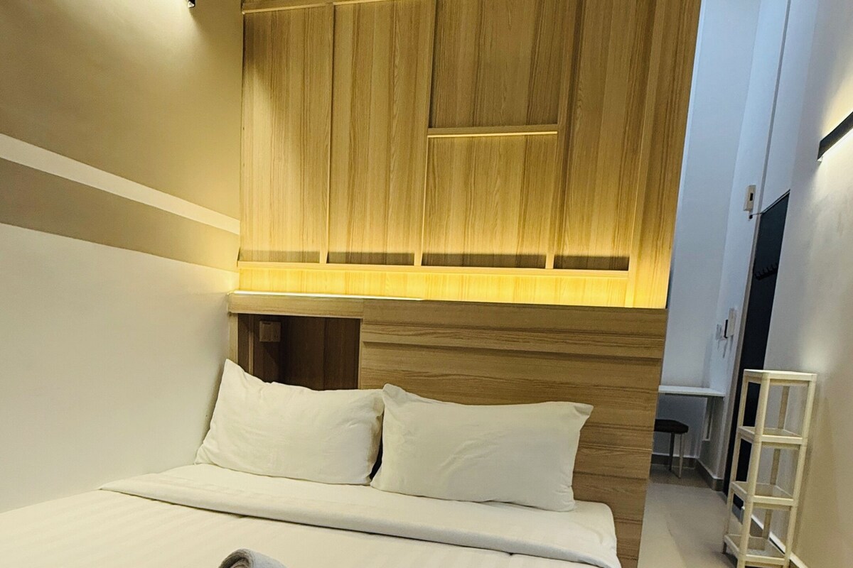 A neatly made bed with a rolled towel, a wooden headboard, and a ceiling fan.