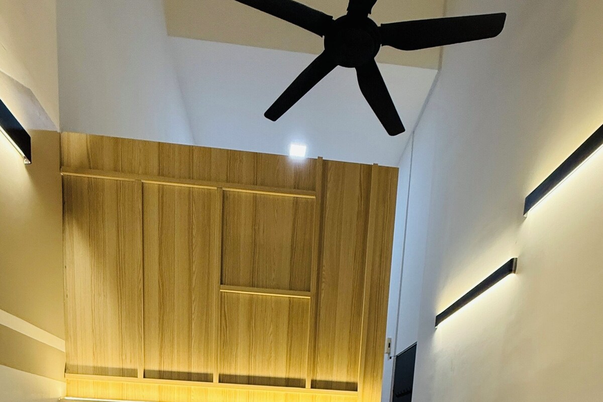 A modern bedroom with a large bed, wooden headboard, ceiling fan, and bedside table.