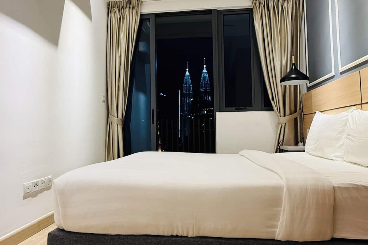 A modern hotel room with a large bed, a view of the cityscape, and a ceiling fan.