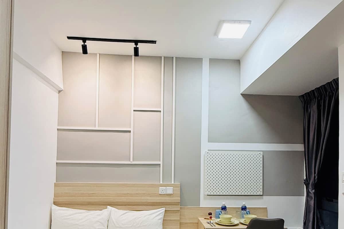 A hotel room with a bed, a desk, a chair, a ceiling fan, a window with curtains, and a wall-mounted light fixture.