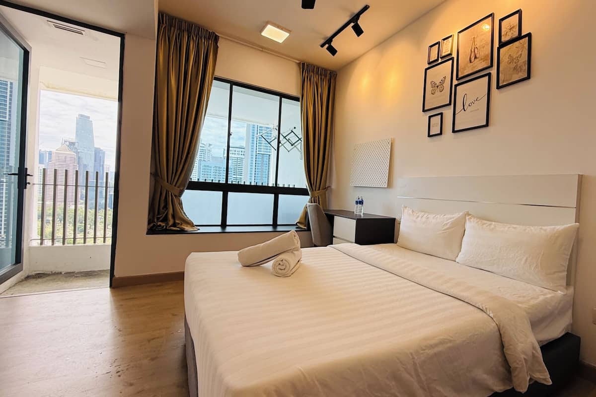 A hotel room with a large bed, a nightstand, a window with curtains, and framed pictures on the wall.